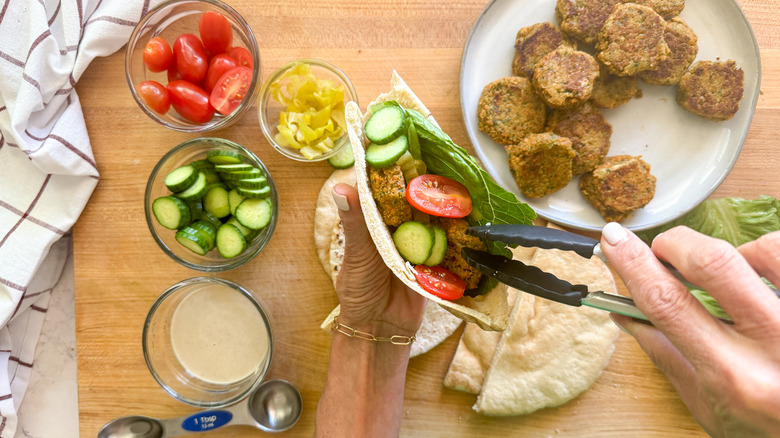 hand adding falafel to pita