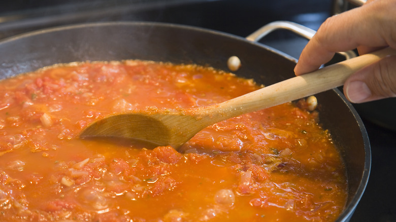 Tomato sauce cooking down in a pan with a wooden spoon dipping in