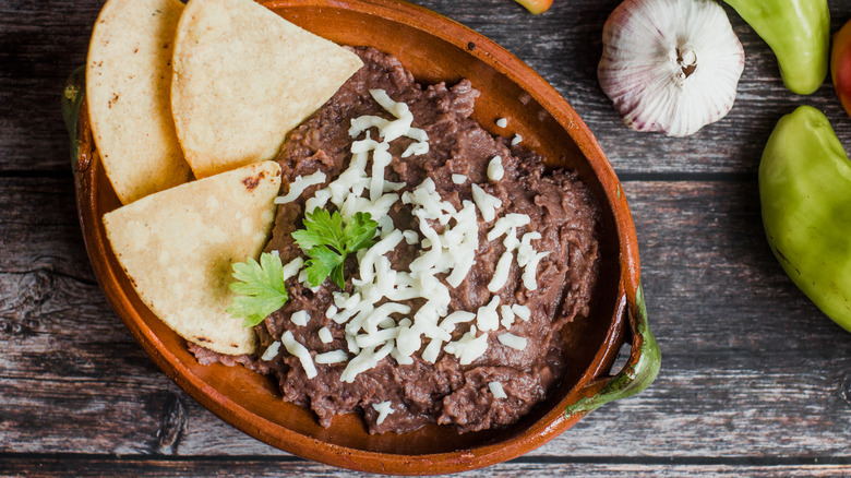 refried beans and tortillas in a clay dish with cheese