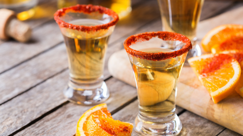 Shots of liquor with a Tajín rim and oranges