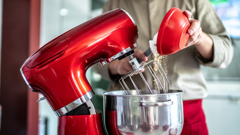 Hands pouring ingredients into stand mixer bowl