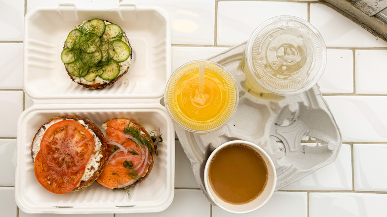 Bagels with cream cheese, cucumbers, tomatoes, and lox with orange juice, coffee, and lemonade on white tile