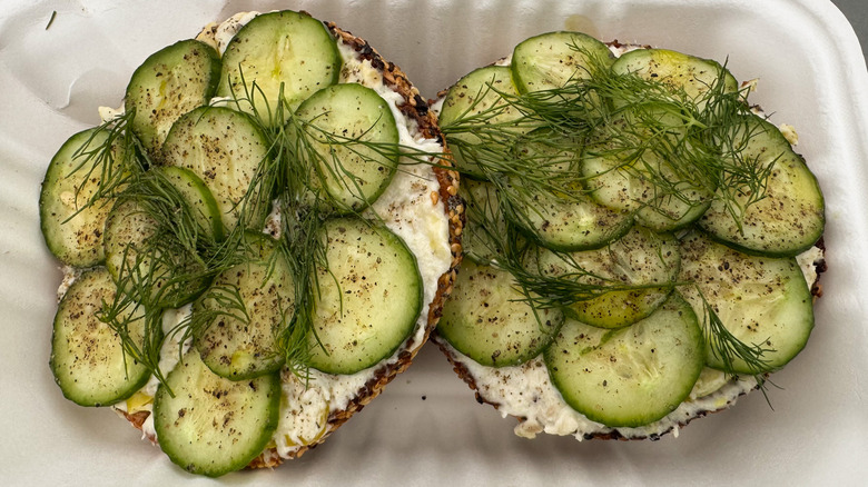 Bagel with white fish spread, cucumbers, and fresh dill in a takeout container