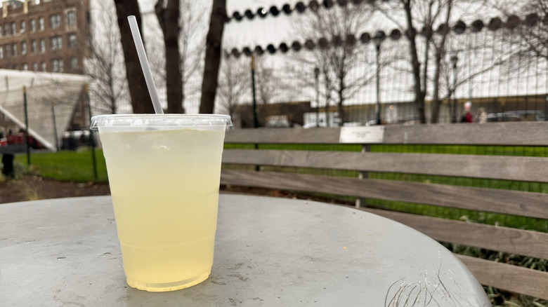 Lemonade in plastic container on a table near a park bench