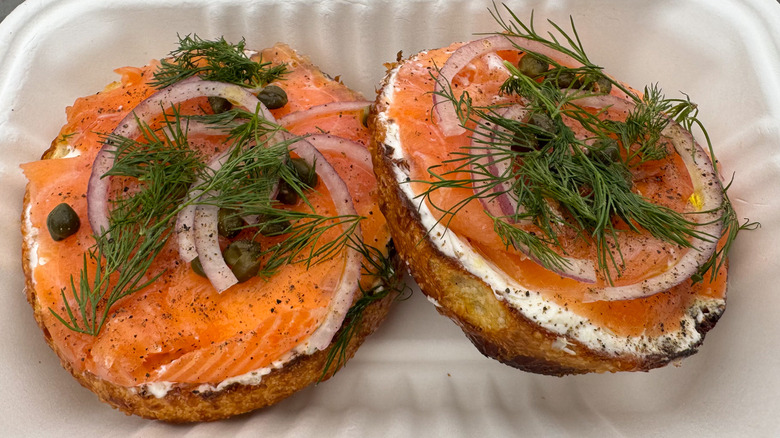 Bagel with smoked salmon, red onion, capers, fresh dill, and cream cheese in a takeout container