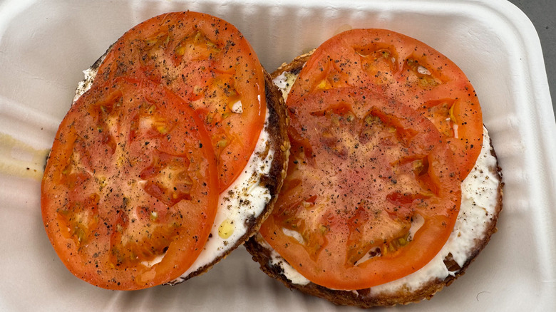 Bagel with cream cheese and tomato in a takeout container