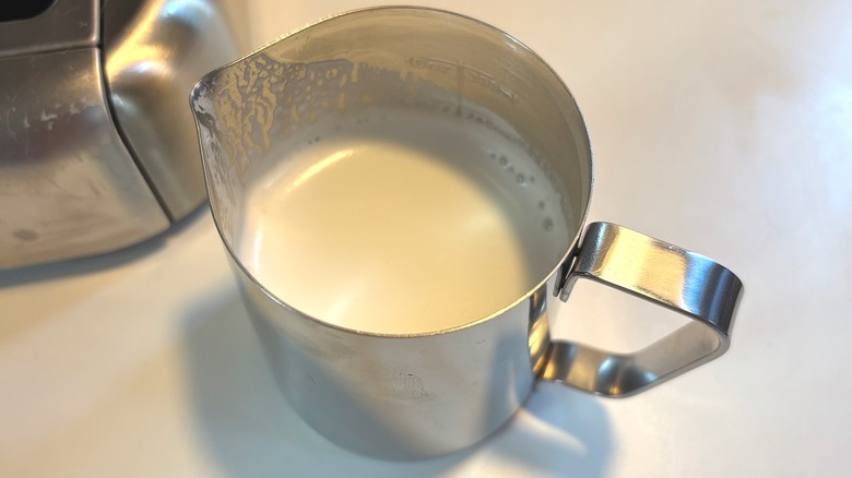 Silver pitcher of steamed milk on white table