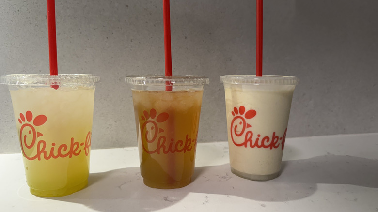 Three Chick-fil-A drink cups with straws on white counter.