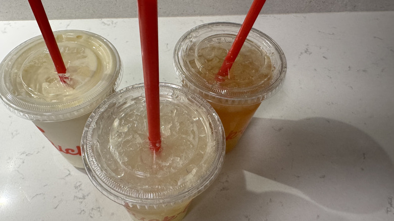 Overhead view of three Chick-fil-A drink cups with straws on white counter.