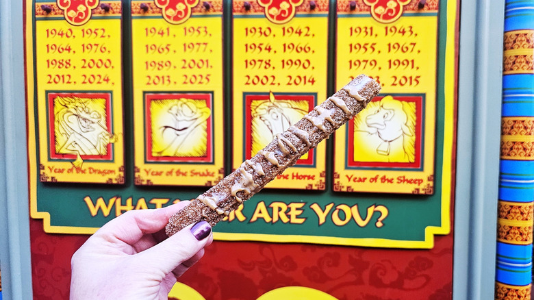 Hand holding a Vietnamese coffee churro in front of a decorative Lunar zodiac sign.