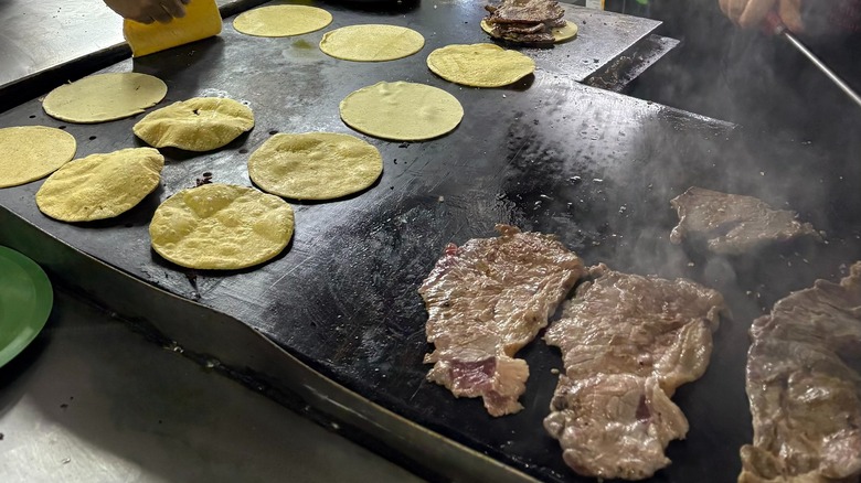 meat and tortillas frying on a grill