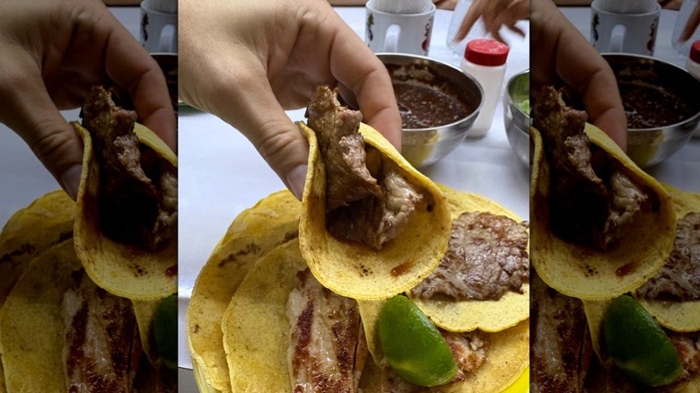 Hand pinching together a meat taco with no salsa