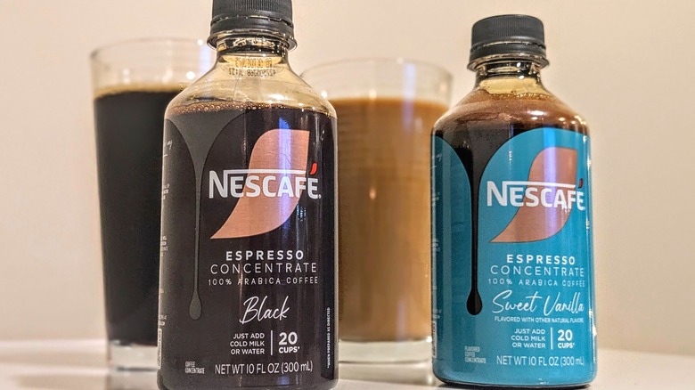 Two Nescafé espresso concentrate bottles with glasses of iced coffee in the background.