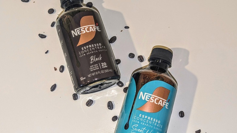 Two bottles of Nescafé espresso concentrate on white background with scattered coffee beans.