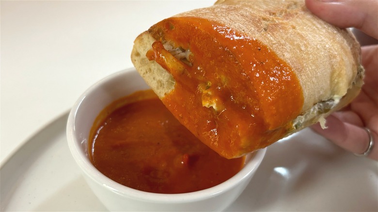 hand holding panera spicy chicken ciabatta dipper dipped in bowl of tomato soup