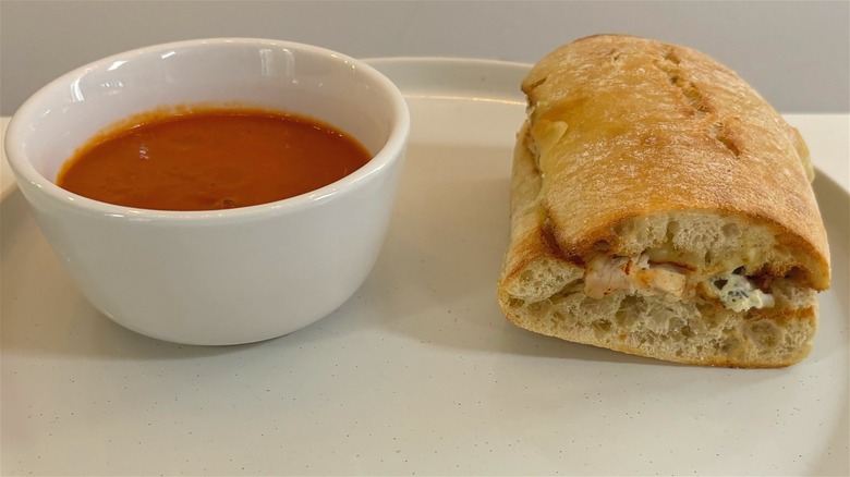 panera spicy chicken ciabatta dipper next to small bowl of tomato soup on white plate