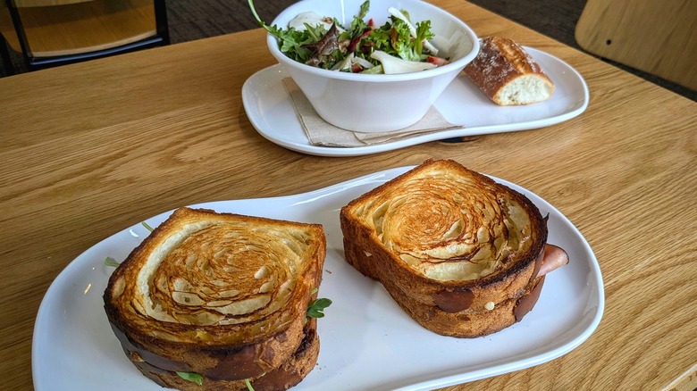 Two croissant toast sandwiches and a salad with baguette on the side on a wood table in a restaurant