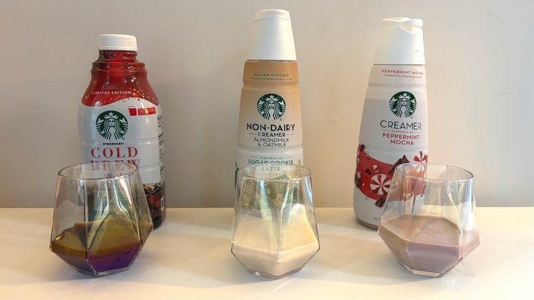 Bottles of Starbucks cold brew concentrate, peppermint mocha creamer, non-dairy sugar cookie latte creamer behind glasses of each beverage on white background