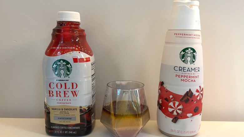 Starbucks cold brew concentrate and peppermint mocha creamer bottles next to glass with coffee and creamer