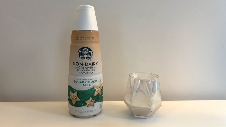 Bottle of Starbucks non-dairy sugar cookie latte creamer next to glass of creamer on white background