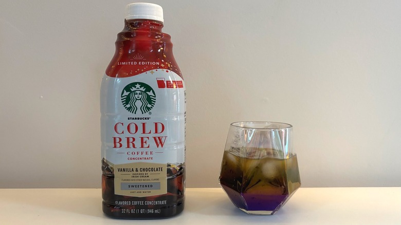 Bottle of Starbucks cold brew coffee concentrate next to glass of cold brew on white background