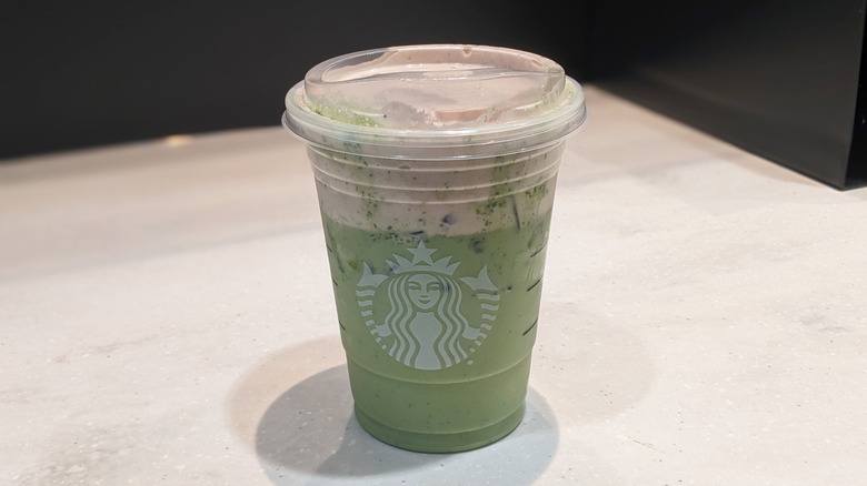 Closed Starbucks takeout cup on a table, holding the Dubai chocolate pistachio matcha latte.