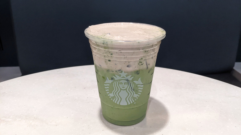 Open Starbucks takeout cup on a table, with a chocolate pistachio matcha latte.