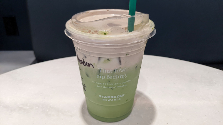 Starbucks takeout cup holding the matcha latte, with a straw.