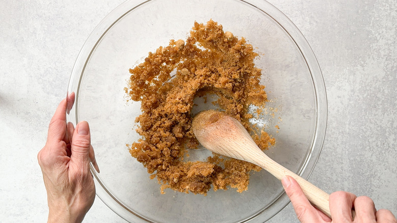 Stirring brown sugar into brown butter in glass bowl with wooden spoon