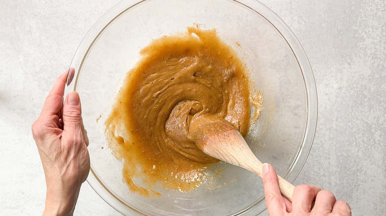 Stirring egg and vanilla into brown sugar and butter in glass bowl with wooden spoon