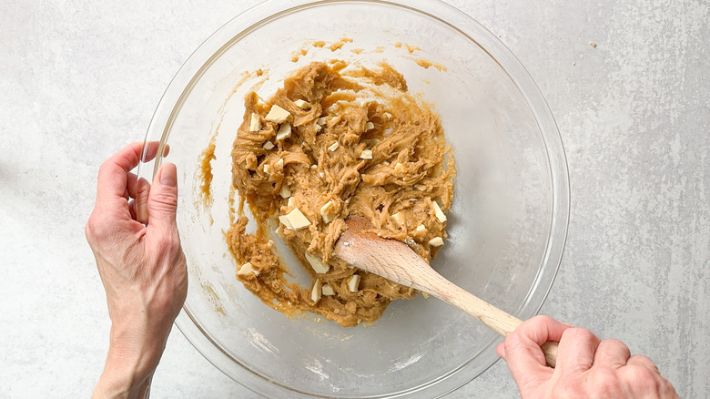 Stirring white chocolate into blondie batter with wooden spoon in glass bowl