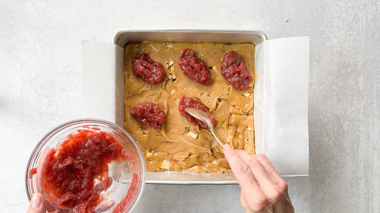 Spooning rhubarb compote onto white chocolate blondie batter in baking pan