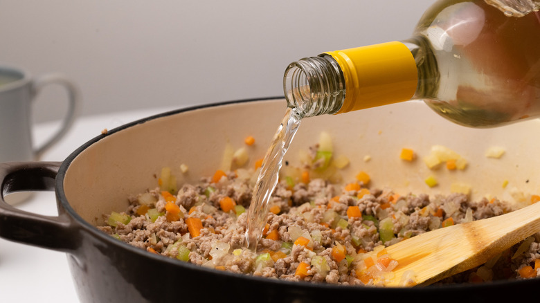 Pouring white wine into bolognese 