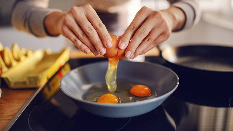 Hands cracking eggs into pan