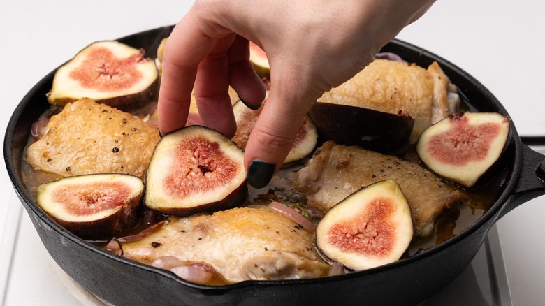 Hand placing figs with chicken in a skillet