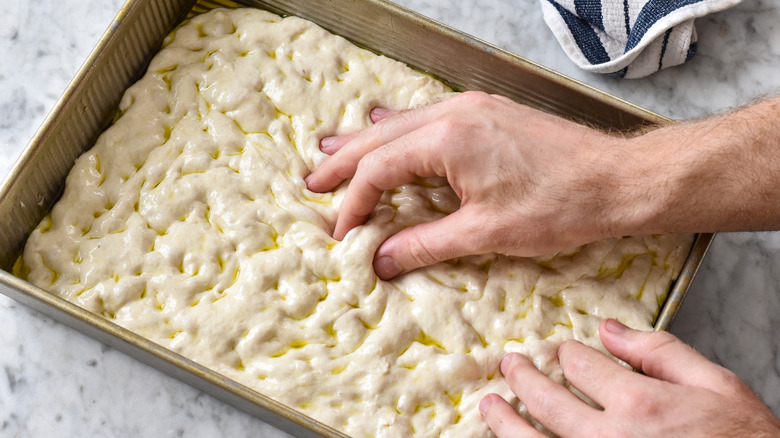 pinching focaccia dough with fingertips