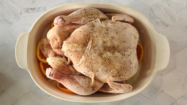 raw chicken in baking dish over oranges and onions