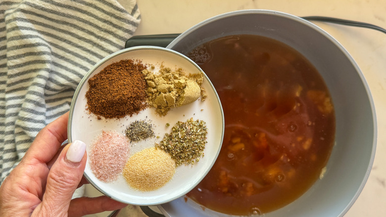 hand adding spices to pot