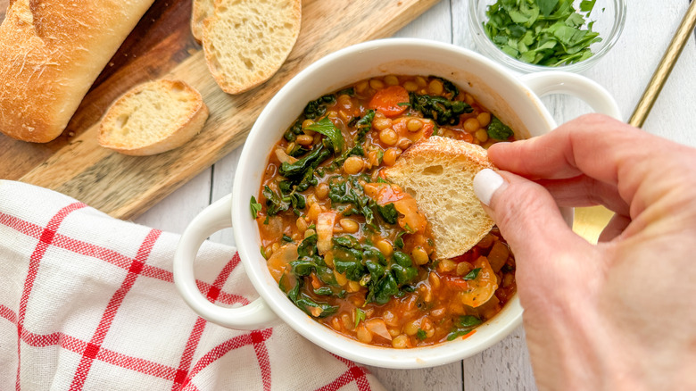 hand dipping bread in kale lentil vegetable soup