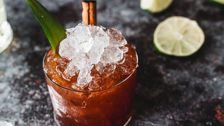 Red cocktail with ice and pineapple leaf, limes in back