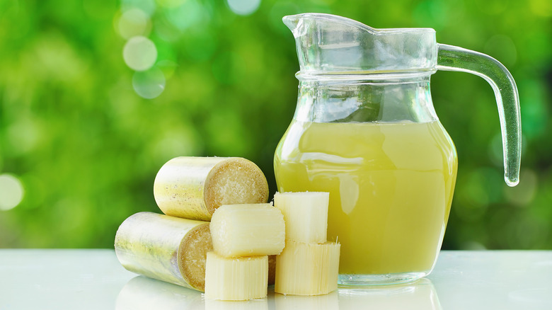 A pitcher of fresh sugar cane juice next to sliced canes