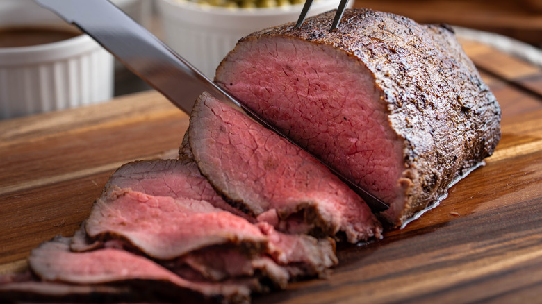 A knife slicing a cooked roast beef rump