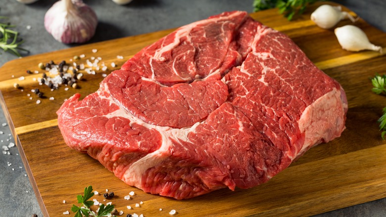 A raw beef chuck roast on a wooden board