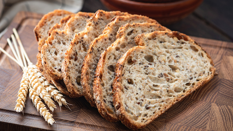 Whole wheat bread slices lined up on a cutting board with a small bundle of wheat