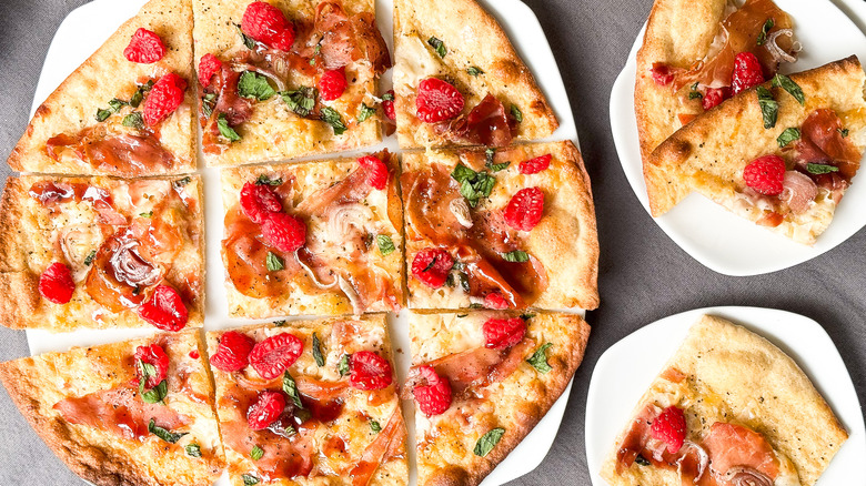 Rye flatbreads with prosciutto and raspberry cut into slices on serving platter with plates