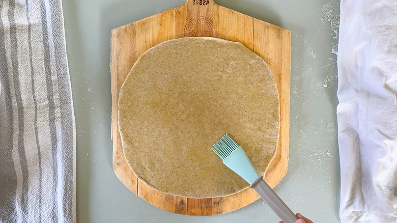Brushing olive oil on flatbread dough on pizza peel