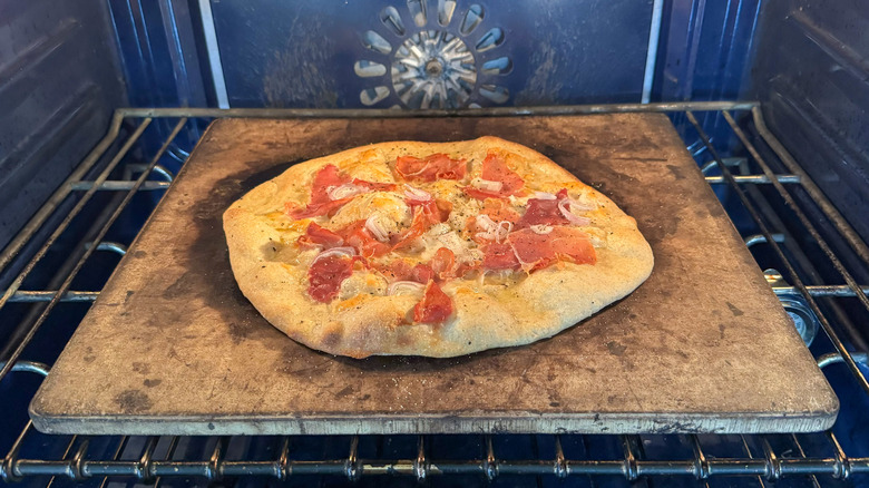 Rye flatbread with prosciutto and raspberry baking on pizza stone in oven