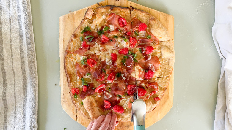 Slicing rye flatbread with prosciutto and raspberry on 