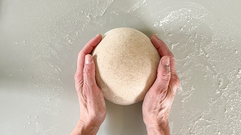 Shaping rye flatbread dough into ball on floured surface