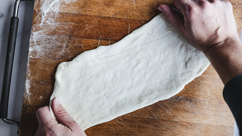 Hands stretching dough on cutting board